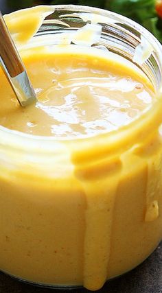 a glass jar filled with yellow liquid sitting on top of a table next to vegetables