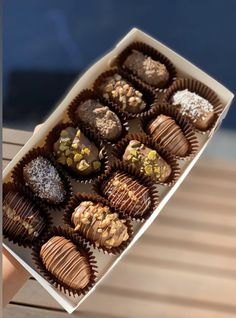 a hand holding a box of chocolates on top of a wooden table next to a window