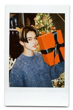 a young man holding up a present box in front of a christmas tree