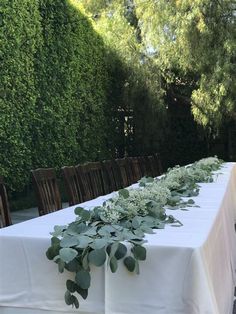 a long table is set up with white linens and greenery