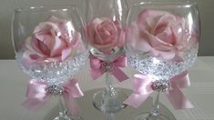 three wine glasses decorated with pink roses and diaper on a white tableclothed surface