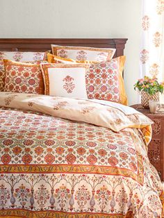 a bed with an orange and white comforter next to a wooden headboard in front of a window