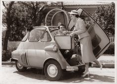 an old photo of two women loading luggage onto a small car in front of a house