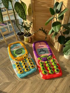 two colorful cell phones sitting next to each other on a wooden floor in front of a potted plant