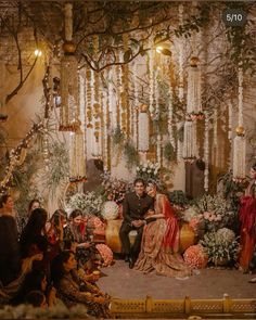 a couple sitting on a stage surrounded by flowers and greenery at their wedding reception