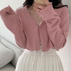 a woman wearing a pink sweater and white pleated skirt