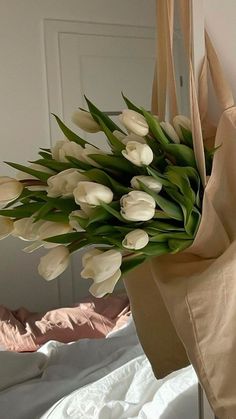 a bouquet of white tulips in a paper bag on a bed with sheets