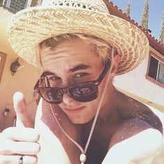 a woman wearing sunglasses and a straw hat giving the thumbs up