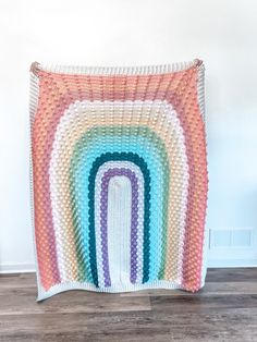 a multicolored crocheted blanket hanging on the wall in front of a wooden floor