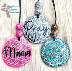 three personalized pendants are shown on a furnishing surface with the word pray and mama written in black ink