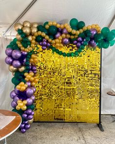 the balloon arch is decorated with gold, purple and green balloons