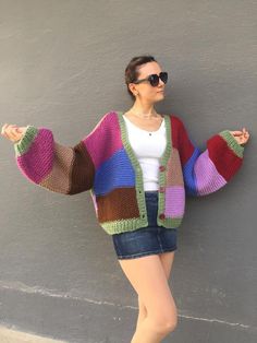 a woman standing next to a wall wearing a colorful cardigan sweater and denim shorts