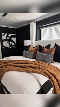 a bedroom with black walls and white bedding, brown throw pillows and blankets on the headboard