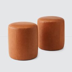 two tan leather stools sitting next to each other on a white surface, one is empty