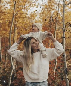 a woman holding her child up in the air while standing next to trees with leaves on them