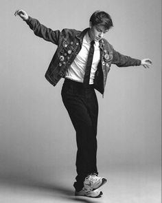 a young man riding a skateboard while wearing a jacket and tie with his arms outstretched