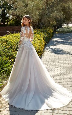 a woman in a wedding dress standing on a brick path with trees and bushes behind her