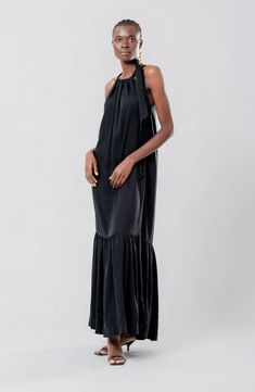 An adjustable tie on the neck means a custom fit in this graceful maxi dress showcasing a flounce hem for added dimension. Each piece is designed for longevity. Every garment is made-to-order to reduce production waste. 57" length Ties at neck Jewel neck Sleeveless, with cutaway shoulders Unlined 100% lyocell Machine wash, line dry Made in Senegal Black Owned/Founded Chic Evening Maxi Dress With Ruffle Hem, Elegant Silk Maxi Dress With Ruffle Hem, Silk Maxi Dress With Ruffle Hem, Silk Maxi Dress For Black-tie Events, Elegant Maxi Dress For Black-tie Events, Chic Halter Neck Maxi Dress With Ruffle Hem, Chic Silk Maxi Dress For Black-tie Events, Black Maxi Dress For Black-tie Events, Black Bias Cut Maxi Dress