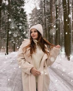 a woman standing in the snow wearing a white coat and hat with her hands on her hips