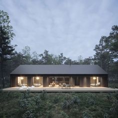 a house in the middle of a forest with lights on it's windows and doors