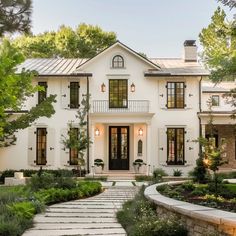 a large white house with lots of windows and plants on the front lawn, surrounded by greenery