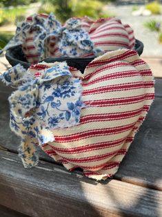 two fabric hearts are sitting on a picnic table outside in the sun, one is red and white with blue flowers