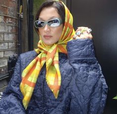 a woman wearing sunglasses and a scarf on her head is holding something in her hand