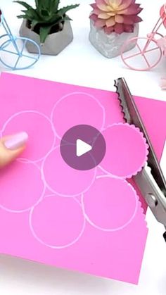 someone is cutting out paper with scissors on top of the pink piece of paper that has been cut into flower shapes