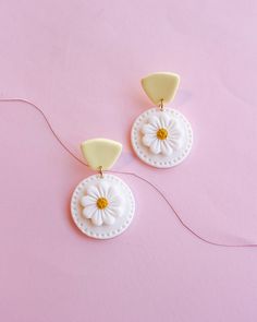 two white and yellow flower shaped earrings on a pink surface with string attached to them