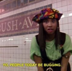 a young woman with long hair wearing a colorful hat in front of a tiled wall