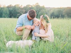 a man kneeling down next to a woman holding a baby in a field with a dog