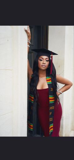 a woman wearing a graduation cap and gown leaning against a wall with her hand on her hip