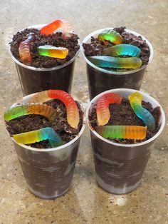 four plastic buckets filled with dirt and colorful worms on top of each other in dirt