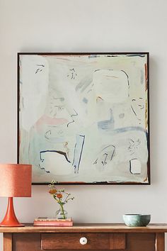 an abstract painting hangs above a wooden table with a lamp on it and a vase in the foreground