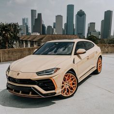 a beige sports car parked in front of a cityscape with orange rims