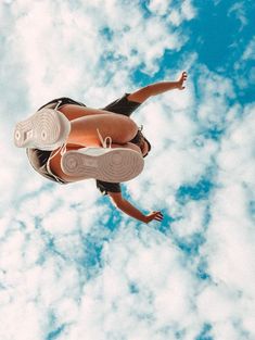 a woman flying through the air while riding a skateboard in front of a cloudy blue sky