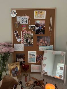 a cluttered desk with flowers and pictures on the bulletin board, candles and other items