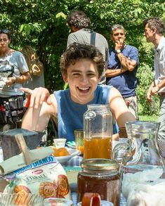 a young man sitting at a table with food and drinks in front of him, surrounded by other people