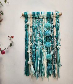 a wall hanging made out of beads and tassels with flowers in the background