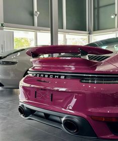 the back end of a pink porsche car in a showroom with other cars behind it