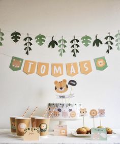 a table topped with cupcakes and cake next to bunting banner that says tomas