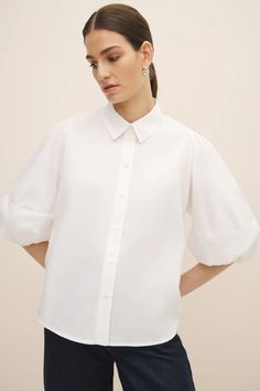 A simple yet sculptural shirt, made from 100% certified Fairtrade organic cotton poplin shirting. The Joan Shirt is defined by sculptural balloon sleeves, and features a neat collar and subtly curved hem. It has a standard fit with neat shoulders and a slight A-line shape through the body. Fastens through the front with agoya shell buttons. Designed for a standard fit, we recommend taking your normal size. Kowtow's model Holly is wearing a size XS. Holly's measurements:Height: 178cm / 5'10.5" Poplin Short Sleeve Workwear Blouse, Short Sleeve Poplin Blouse For Work, Chic Poplin Top With Relaxed Fit, Daywear Shirt With Puff Sleeves, Chic Cotton Shirt With Gathered Sleeves, Puff Sleeve Blouson Shirt For Daywear, Formal Tops With Puff Sleeves And Cuffed Details, Spring Cotton Shirt With Blouson Sleeves, Classic Workwear Top With Balloon Sleeves