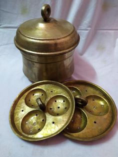 three brass dishes with lids on a white tablecloth