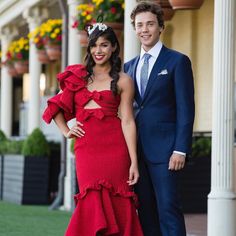 a man and woman in formal wear standing next to each other on the grass outside of a building