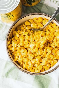 a bowl filled with corn sitting on top of a table next to cans of food