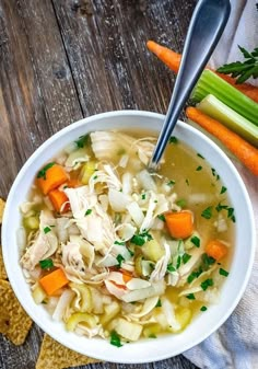 a white bowl filled with chicken noodle soup next to carrots and celery