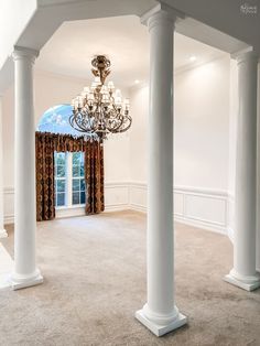 a chandelier hangs from the ceiling in an empty room with columns and curtains