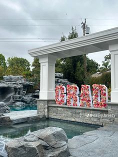 there is a sign with flowers on it in front of a pool and some rocks