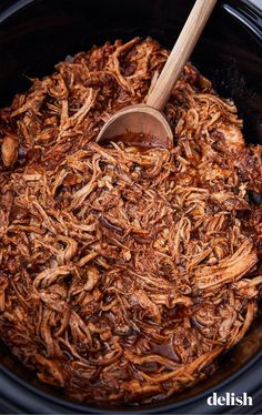 shredded pulled pork in a slow cooker with a wooden ladle scooping it out