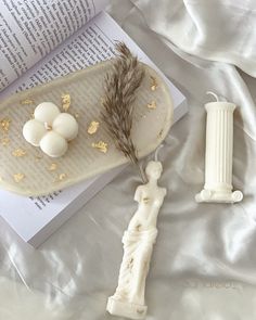 an open book on a bed next to some figurines and a candle holder